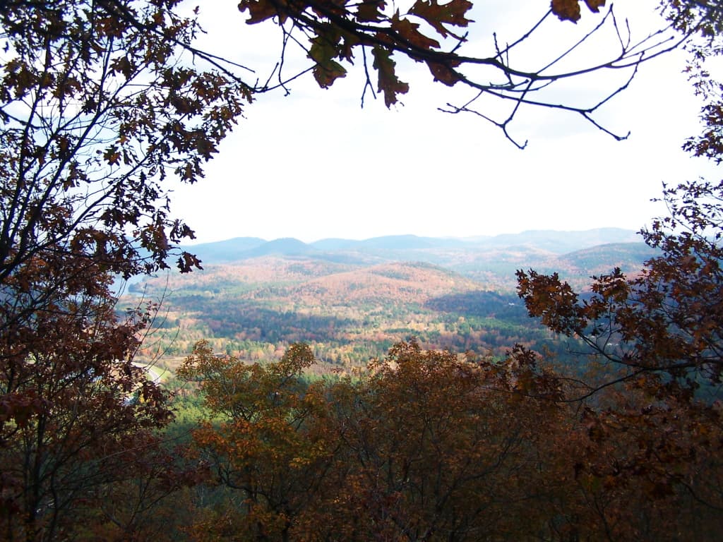 Autumn trees frame a wide view across layered forested Adirondack hills.